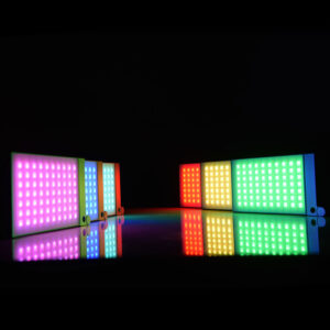 Godox M1 Mobile RGB LED -valaisin - Harmaa heijastaa eloisat vaaleanpunaiset, violetit, siniset, keltaiset, punaiset ja vihreät valot mustalle taustalle luoden värikkäitä heijastuksia alla olevalle kiiltävälle pinnalle.