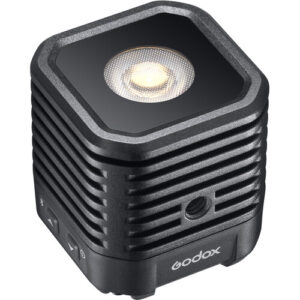 1617973841_909 Godox WL4B Waterproof LED-valaisin on kompakti, musta, kuution muotoinen LED-valaisin, jossa on kuvioitu pinta, tuuletusaukot, sivusäätöpainikkeet ja pyöreä valopaneeli yläosassa.