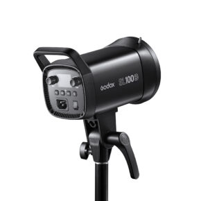 1621500353_528 Musta Godox LED SL100D Daylight -LED-valo on asennettu jalustalle, ja se on kuvattu kulmassa, jossa näkyy sen ohjauspaneeli, säätönupit ja kahva.