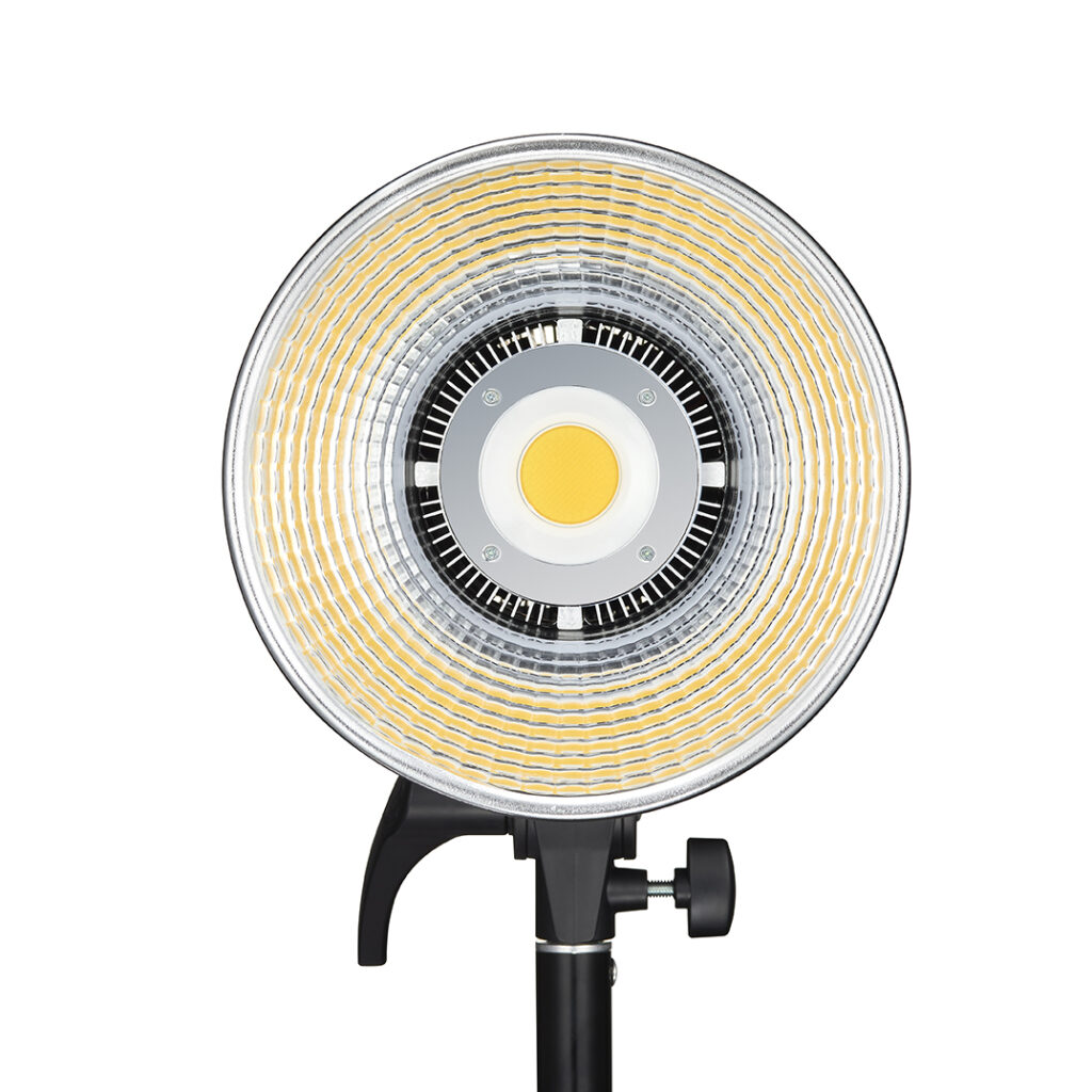 1621500381_593 Godox LED SL100D Daylight on pyöreä LED-valaisin, jossa on keskittyvät keltaiset ja hopeiset renkaat ja joka on asennettu mustaan säädettävään jalustaan. Kuvassa edestä valkoista taustaa vasten.