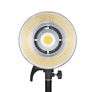 1621500381_593 Godox LED SL100D Daylight on pyöreä LED-valaisin, jossa on keskittyvät keltaiset ja hopeiset renkaat ja joka on asennettu mustaan säädettävään jalustaan. Kuvassa edestä valkoista taustaa vasten.