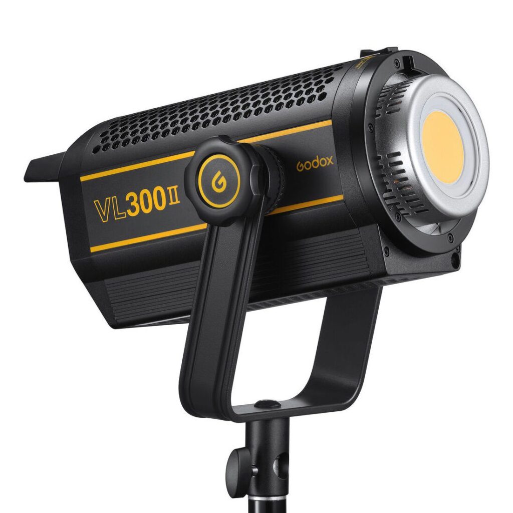 Mustakeltainen Godox VL300II LED-videovalaisin -LED-valo on asennettu jalustalle, ja sen rungossa on virtapainike ja suuret jäähdytysaukot.