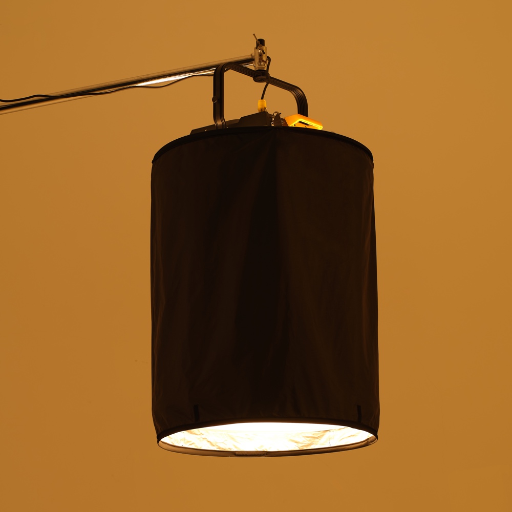 1689769159_959 Godox P600BHSSS Black Opaque Skirt for P600Bi Hard peittää sylinterimäisen studiovalon, joka roikkuu metallisesta varresta ja heittää lämpimän alaspäin suuntautuvan valon kellanruskeaa taustaa vasten.