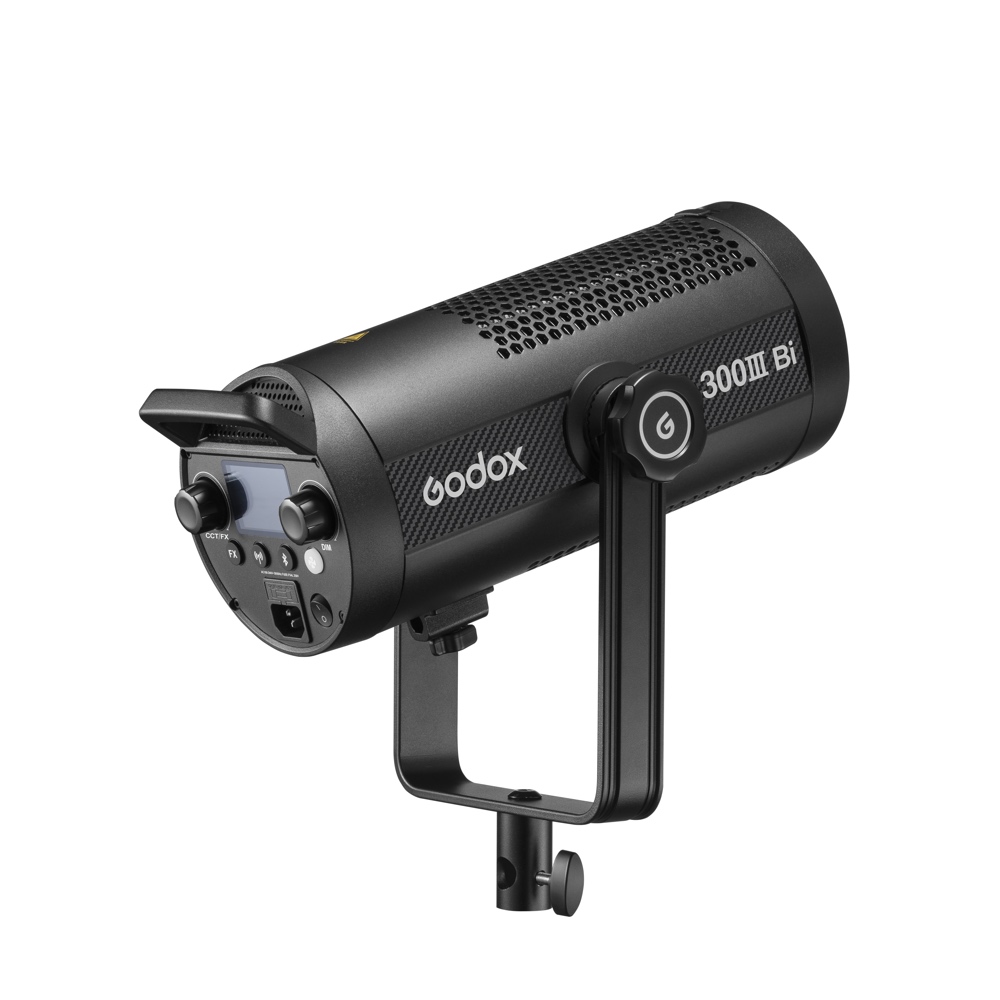1692103364_167 Musta Godox SL300IIIBi Bi Color LED Light -LED-valo (300W), jossa on ohjauspainikkeet, näyttö ja tuuletettu runko, on asennettu joke-kannattimeen ja näytetään valkoista taustaa vasten.