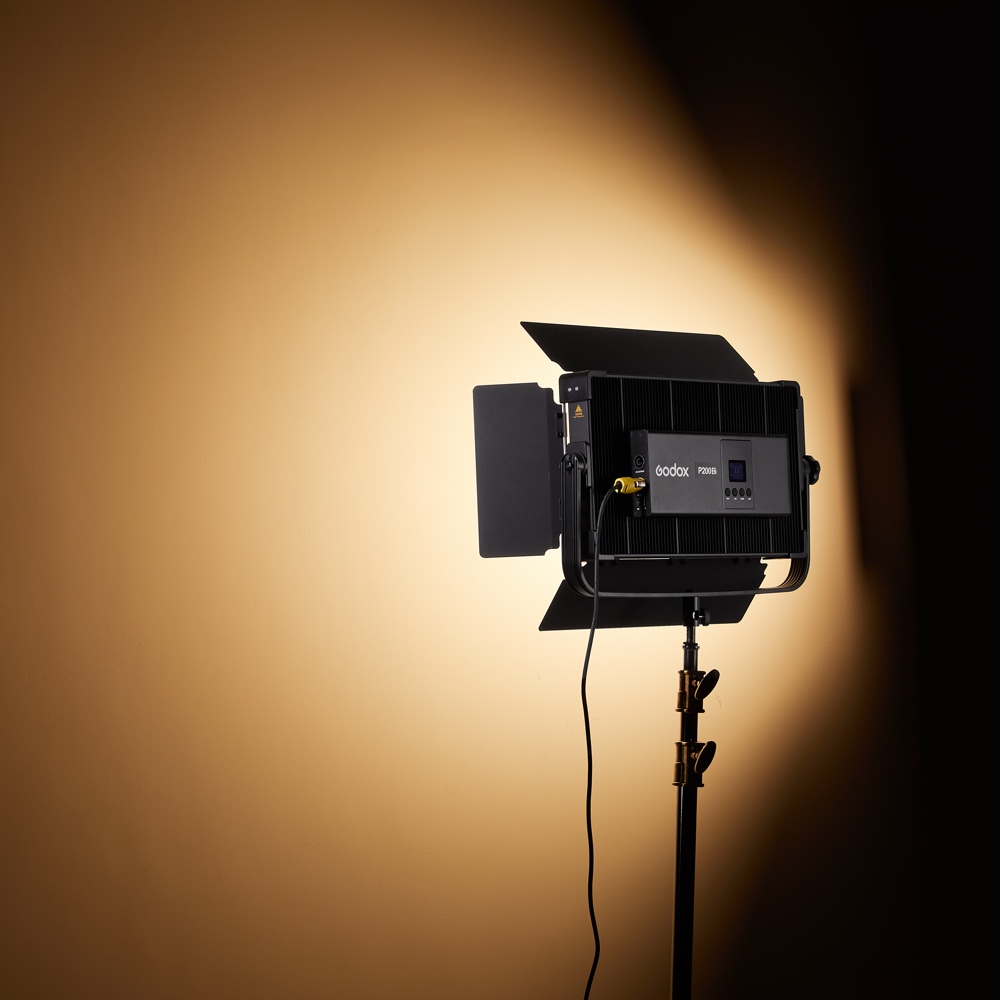 1704806425_343 Godox P200BI Studio LED-valopaneeli ladonluukuilla on kytketty päälle, asennettu jalustalle ja säteilee kirkkaan, fokusoidun valonsäteen tavalliselle beigelle seinälle valokuvaus- tai videostudiossa.