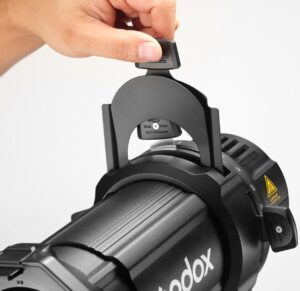 1706182624_376 Käsi säätää Godox Spotlight Attachment MLP26K:ta ML30/ML60-studiovaloille, joka on asennettu valon päälle valkoista taustaa vasten.