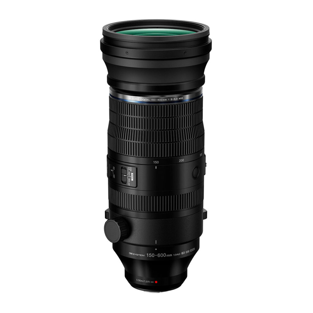 OM_150-600mm_002 OM System M.Zuiko Digital ED 150-600mm f/5.0-6.3 IS -objektiivi seisoo pystyasennossa valkoisella taustalla, ja siinä on näkyvät säätökytkimet, tarkennusrengas, jalustapanta ja polttovälimerkinnät 150mm:stä 600mm:iin.
