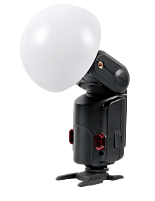 1388216355_449 Godox Witstro Diffusor Ball, suuri valkoinen kupolimuotoinen kamerasalaman diffuusori, on kuvassa kiinnitettynä salamalaitteeseen ja asennettuna pieneen mustaan jalustaan valkoista taustaa vasten.