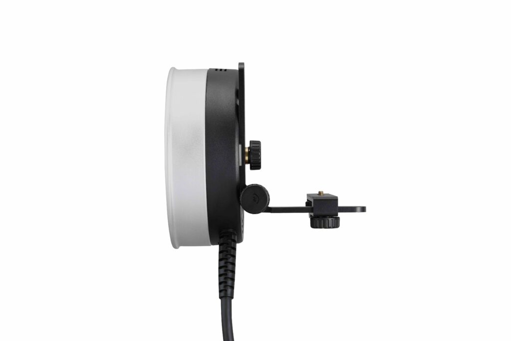 Sivunäkymä Godox R1200 -rengassalamapäästä AD1200Pro:lle, jossa on pyöreä muotoilu mustalla ja hopeisella kehyksellä, kiinnitetty kiinnike ja virtajohto, joka ulottuu alaspäin valkoista taustaa vasten.