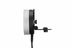 Sivunäkymä Godox R1200 -rengassalamapäästä AD1200Pro:lle, jossa on pyöreä muotoilu mustalla ja hopeisella kehyksellä, kiinnitetty kiinnike ja virtajohto, joka ulottuu alaspäin valkoista taustaa vasten.