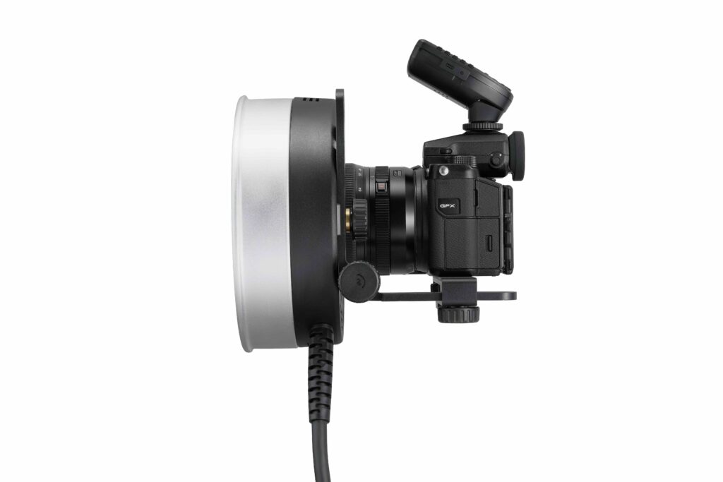 Godox R1200 -rengassalamapää AD1200Pro:lle on kuvassa mustana, ja sen etupuolelle on asennettu suuri rengassalama, sivulta katsottuna valkoista taustaa vasten. Rengassalamaan on liitetty virtajohto.