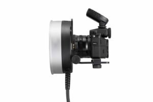 Godox R1200 -rengassalamapää AD1200Pro:lle on kuvassa mustana, ja sen etupuolelle on asennettu suuri rengassalama, sivulta katsottuna valkoista taustaa vasten. Rengassalamaan on liitetty virtajohto.