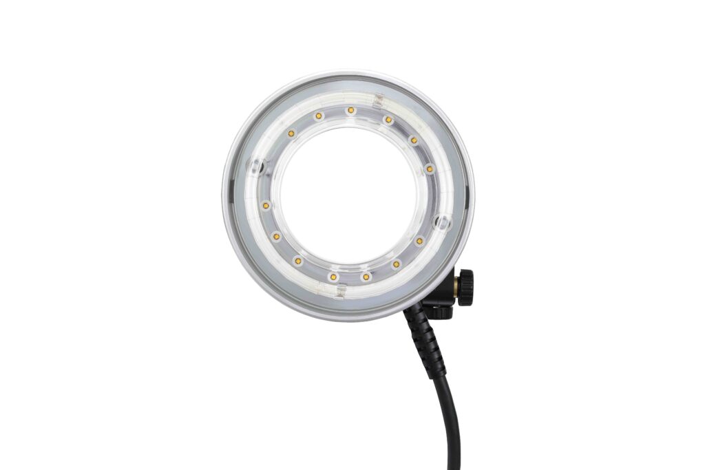Lähikuvassa Godox R1200 Ring Flash Head for AD1200Pro -salamavalaisimesta näkyy sen pyöreä LED-muotoilu, läpinäkyvä ulkokotelo, keskiaukko ja sivuvirtajohto, kaikki valkoista taustaa vasten.