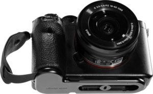 800q-01_124043 Musta Sony peilitön kamera, jossa on 16-50 mm:n objektiivi, on kuvassa ylhäältä alaspäin kiinnitettynä mustaan Peak Design Micro Clutch L-Plate -laattaan, jossa on rannehihna. Objektiivin yksityiskohdat ja kameran säätimet ovat näkyvissä.
