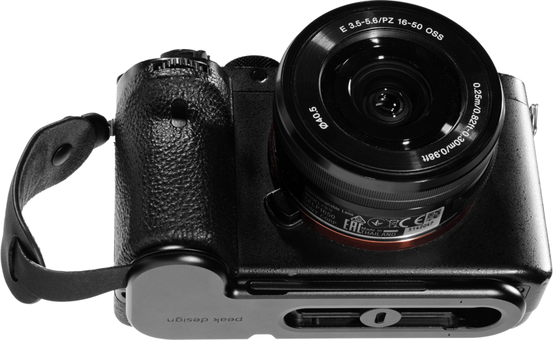 800q-01_124043 Musta Sony peilitön kamera, jossa on 16-50 mm:n objektiivi, on kuvassa ylhäältä alaspäin kiinnitettynä mustaan Peak Design Micro Clutch L-Plate -laattaan, jossa on rannehihna. Objektiivin yksityiskohdat ja kameran säätimet ovat näkyvissä.