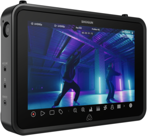 ATOMOS SHOGUN 7-tuumaisen HDR Monitor-Recorder 6K RAW -näytön lähikuvassa näkyy kaksi ihmistä tanssimassa värikkäässä, neonvalaistussa teollisuusympäristössä, ja kameran asetukset ja ohjauskuvakkeet näkyvät sen näytöllä.
