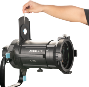 800q-02_117968 Henkilön käsi asettaa metallisen gobon mustan NANLITE PJ-BM-AI Adjustable Iris -projektorivalon aukkoon valkoista taustaa vasten.