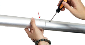 800q-03_122084 A person uses a screwdriver to tighten a screw that connects two NANLITE Background Tube 3-meter tubes; one hand holds the tube while the other turns the screwdriver, the red arrow points to the screw.