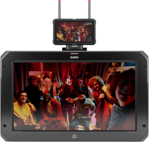 800q-03_125019 Pieni ATOMOS Z-Mount -monitori on isomman näytön päällä, ja molemmissa näkyy iloinen joukko ihmisiä poseeraamassa ja hymyilemässä lämpimästi valaistussa huoneessa, ja joillakin on kädessään soittimia.