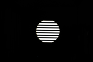 800q-04_117077 NANLITE GOBO Set 1 for PJ-FMM heijastaa kirkasta valkoista valoa vaakasuorilla säleillä varustetun pyöreän ikkunan läpi, jolloin pyöreän muodon sisällä olevat raidalliset kuviot näkyvät pimeässä huoneessa.