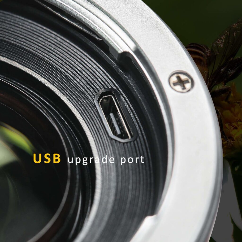1547044529_292 Lähikuva Viltrox EF-FX2 Autofocus Adapter 0,71x -objektiivin kiinnikkeestä, jossa korostuu keltaisella ja valkoisella merkitty USB-päivitysportti, jossa on näkyviä metalli- ja lasiosien yksityiskohtia.