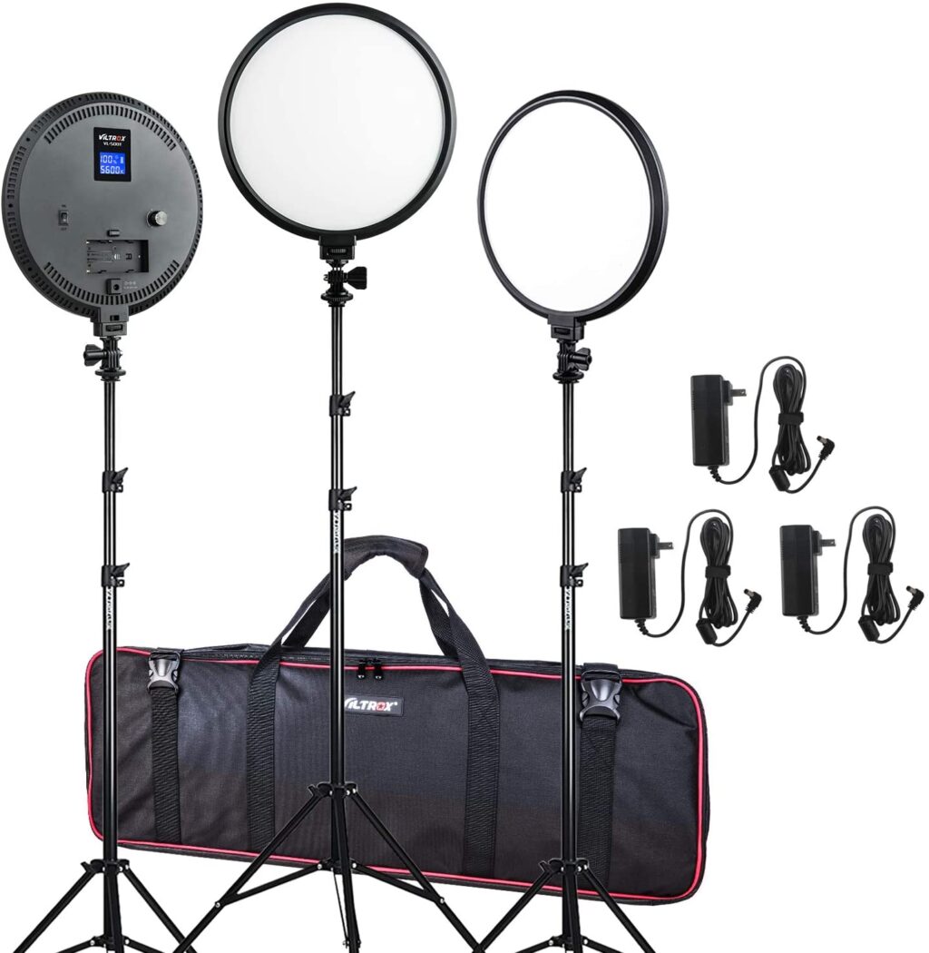 1606309365_527 Viltrox VL 500T LED Light Triple Kit sisältää kolme pyöreää LED-studiovaloa säädettävällä jalustalla, mustan kantolaukun punaisella reunuksella ja neljä virtasovitinta johtoineen, kaikki kuvassa valkoista taustaa vasten.