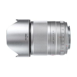 Hopeinen Viltrox AF 33mm f/1.4 -objektiivi Fuji X:lle, jossa on harjattu tarkennusrengas, aukkomerkinnät ja kiinnitetty huppu, kuvattuna sivulta valkoisella taustalla.