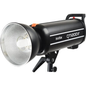 1637154278_243 Musta Godox QT1200II M -studiostroboskooppivalaisin, jossa on hopeinen heijastin ja joka on asennettu pieneen säädettävään kiinnikkeeseen. Siinä on sivukahva ja näkyvä Godoxin tuotemerkki.