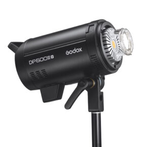 1656492518_033 The black Godox DP600III-V studio strobe is mounted on a stand, with its LED lamp, side cooling valves and control panel visible against a white background.