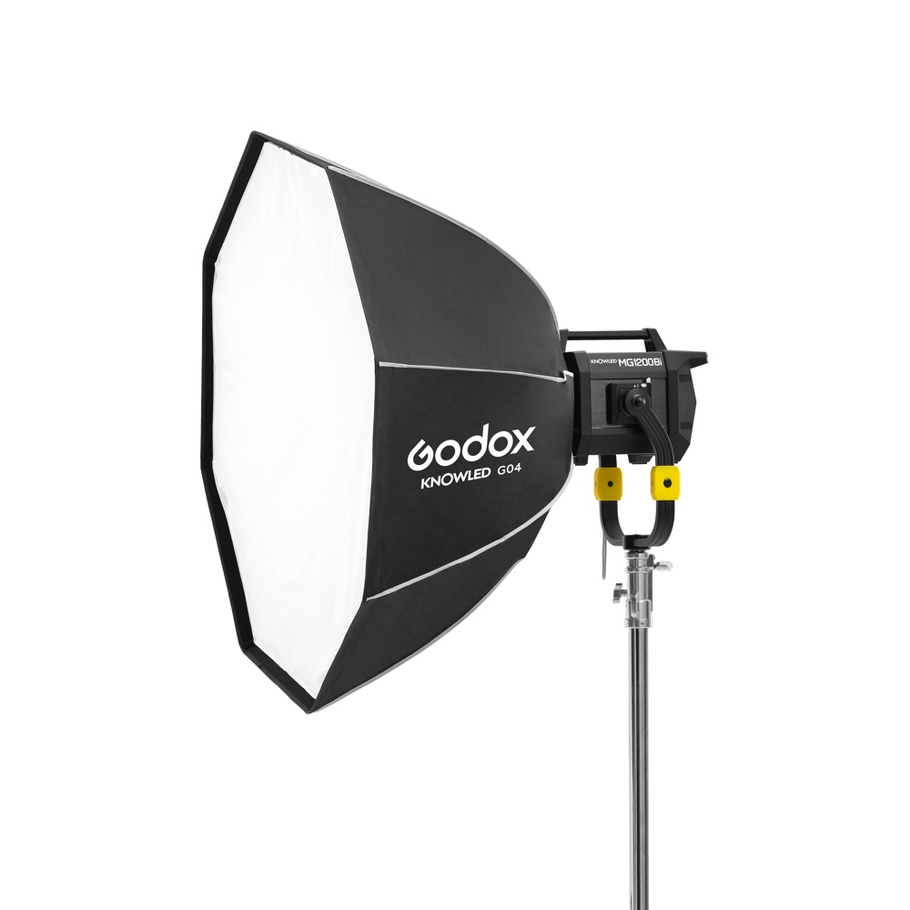 1678977060_191 Ammattikäyttöön tarkoitettu Godox GO4 Octa Softbox 120cm KNOWLED MG1200Bi -valaisimelle on asennettu jalustalle ja suunnattu vasemmalle valkoista taustaa vasten.