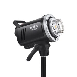 1682497679_127 The black Godox MS200V studio strobe is mounted on a light stand, slightly angled upwards, with visible controls and a circular flash tube at the front.