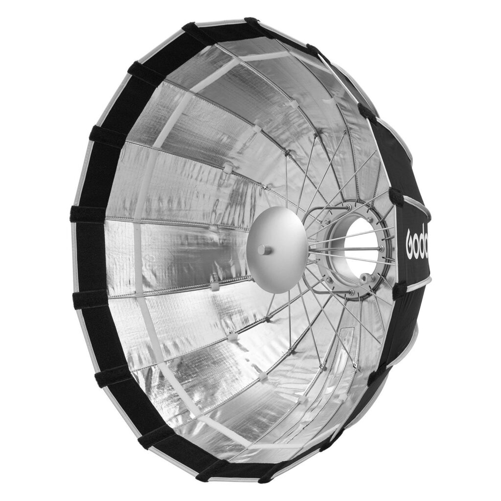 1705321663_934 Godox Multifunctional Softbox S65T on suuri, hopeanvärinen, pyöreä parabolinen heijastin, jossa on metallitangot ja musta reunus studiovalaistukseen. Sivussa on sana "Godox".