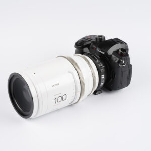 1709809410_923 Musta Panasonic Lumix GH6 -kamera, jossa on suuri valkoinen Viltrox 100mm T2.0 -kino-objektiivi, on kiinnitetty Viltrox PL - MFT -sovittimella, ja kaikki on asetettu valkoista taustaa vasten.