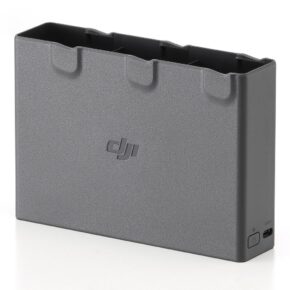 Avata2_010 DJI Avata 2 Two-Way Charging Hub -lataustelakka on harmaa latauskeskitin, jossa on paikat kolmelle akulle, DJI:n logo etupuolella sekä USB-C-portti ja virtapainike sivussa, kuvassa valkoisella pinnalla.