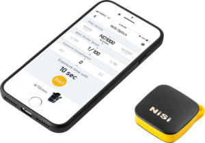 800q-01_117171 Älypuhelin, jossa on valokuvaussovellus, jossa näkyy suodattimen ja valotuksen säätimet, on kompaktin, mustakeltaisen NiSi Remote Control Bluetooth -laitteen vieressä.
