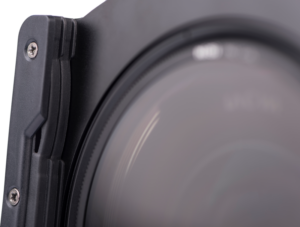Lähikuva Nisi Filter Holder Kit for Laowa 12mm f/2.8 -suodattimen pidikesarjasta kiinnitettynä objektiiviin, jossa näkyy objektiivin lasi, metallikehys ja suodattimen pidikkeen näkyvät ruuvit.