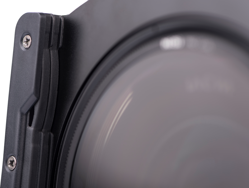 Lähikuva Nisi Filter Holder Kit for Laowa 12mm f/2.8 -suodattimen pidikesarjasta kiinnitettynä objektiiviin, jossa näkyy objektiivin lasi, metallikehys ja suodattimen pidikkeen näkyvät ruuvit.