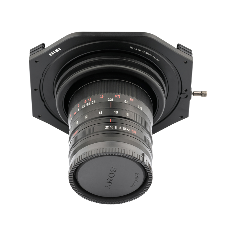 800q-02_110973 Lähikuva Sony-kameran objektiivista, johon on asennettu NiSi-suodatinpidike (100mm) Laowa 10-18mm f/4.5-5.6 -levysuodin pidike, jossa näkyy aukon ja tarkennuksen merkinnät punaisella ja valkoisella valkoista taustaa vasten.