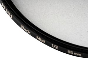 800q-02_119703 Lähikuva NiSi-suodattimesta Black Mist 1/2 95mm -diffuusiosuodin, jossa korostuu sen musta reunus ja hienojakoinen lasipinta vaaleaa taustaa vasten.