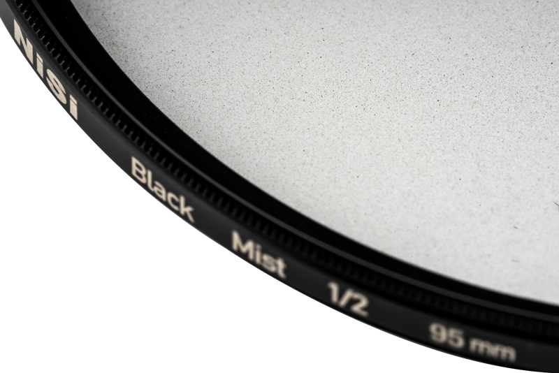 800q-02_119703 Lähikuva NiSi-suodattimesta Black Mist 1/2 95mm -diffuusiosuodin, jossa korostuu sen musta reunus ja hienojakoinen lasipinta vaaleaa taustaa vasten.