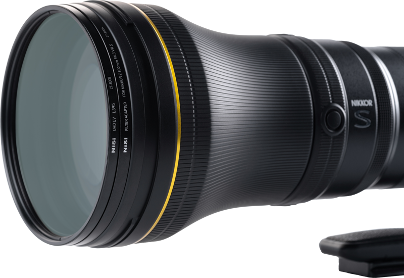 Lähikuva NiSi Filter UHD UV L395 -suodattimesta, joka on kiinnitetty Nikkor Z 800mm f/6.3 VR S -objektiiviin, jossa näkyy sen kuvioitu musta runko, kultainen rengas etuelementin lähellä ja NIKKOR S -brändi sivulla.