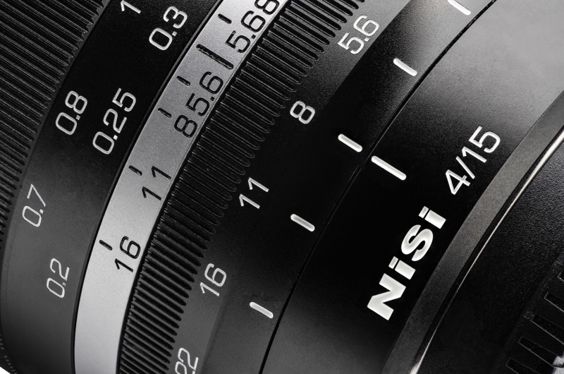 800q-03_115650 Lähikuva mustasta NiSi 15mm f/4 L-Mount -objektiivista, jossa näkyy yksityiskohtaiset tarkennus- ja aukkomerkinnät numeroineen ja yksikköineen sekä näkyvät kuvioidut pitorenkaat.