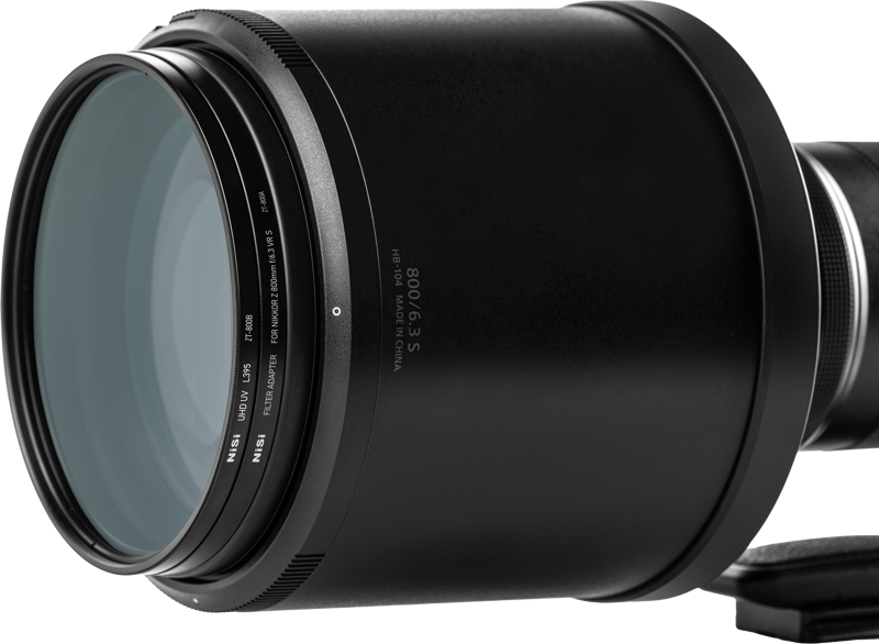 Lähikuva NiSi-suodattimesta UHD UV L395 Nikkor Z 800mm f/6.3 VR S:lle, jossa näkyy yksityiskohtainen teksti reunassa ja näkyvät lasielementit tavallista taustaa vasten.