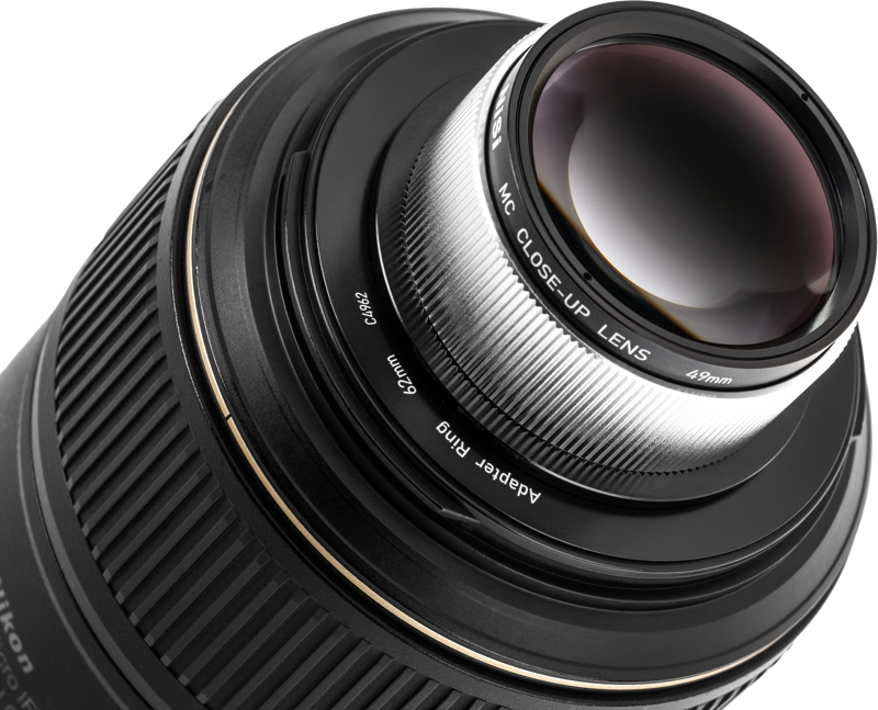 Lähikuva NiSi Close Up Lens Kit NC 49mm -lähilinssi kiinnitettynä kameran objektiiviin sovitinrenkaalla, korostaen objektiivin ja metalliosien yksityiskohtaisia kuvioita.