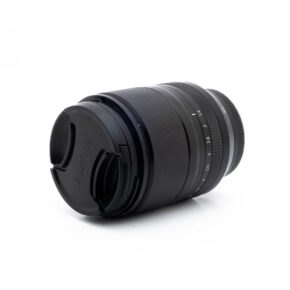 Musta Fujinon XF 23mm f/1.4 R LM WR (sis.ALV24%) - Käytetty -objektiivi, jossa on suojus, on kuvattu kyljellään valkoista taustaa vasten, ja siinä on tarkennusrengas ja zoomausrengas sekä merkittyjen aukonumeroiden numerot rungossa.