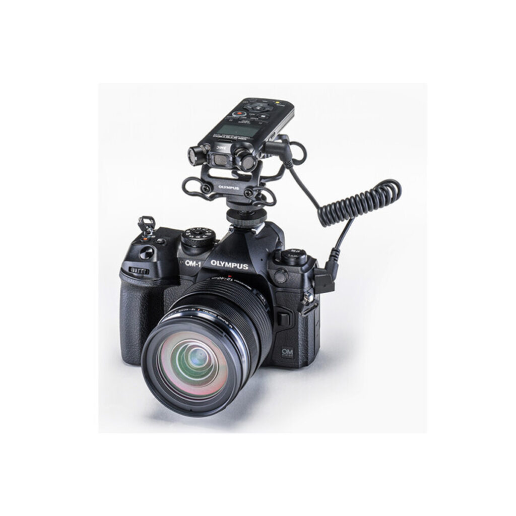 LS-P52 An Olympus OM-D digital camera with a large lens and an OM SYSTEM LS-P5 audio recorder mounted on top with a coiled cable against a white background.