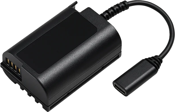 Panasonic BLK22 Dummy Battery USB-C, musta suorakaiteen muotoinen sovitin, jonka toisessa päässä on metallikoskettimet ja johon on liitetty USB-C-kaapeli, näkyy valkoisella pohjalla.