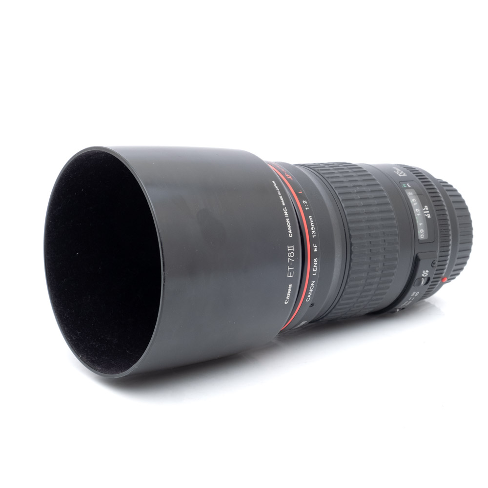 Canon 135mm f2L-1 Musta Canon EF 135mm f/2 L USM - Käytetty kameran objektiivi, johon on kiinnitetty vastavalosuoja, valkoisella taustalla.