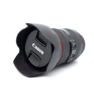 Canon 24-105mm f4L IS USM-1 Canon EF 24-105mm f/4 L IS USM - Käytetty -objektiivi, jossa on punainen rengas, säätökytkimet ja sekä vastavalosuoja että suojus kiinnitettynä, näkyy valkoisella taustalla.