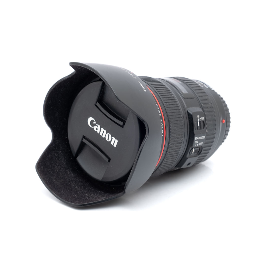 Canon 24-105mm f4L IS USM-1 Canon EF 24-105mm f/4 L IS USM - Käytetty -objektiivi, jossa on punainen rengas, säätökytkimet ja sekä vastavalosuoja että suojus kiinnitettynä, näkyy valkoisella taustalla.